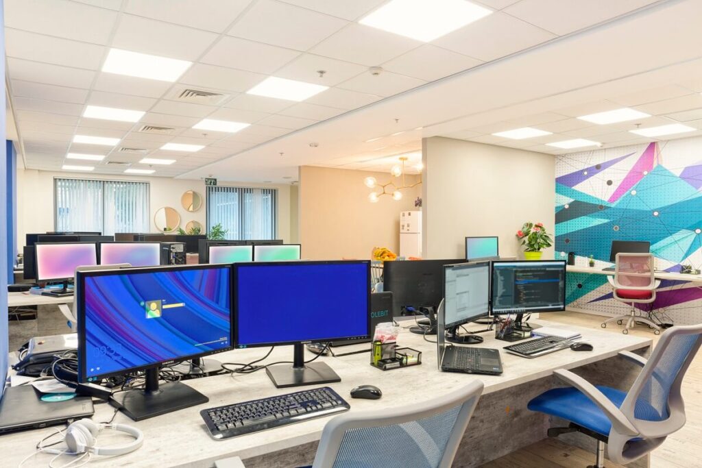 משרד מרווח עם שורות של מחשבים אישיים על שולחנות עבודה, כיסאות משרד וכמה קישוטים.