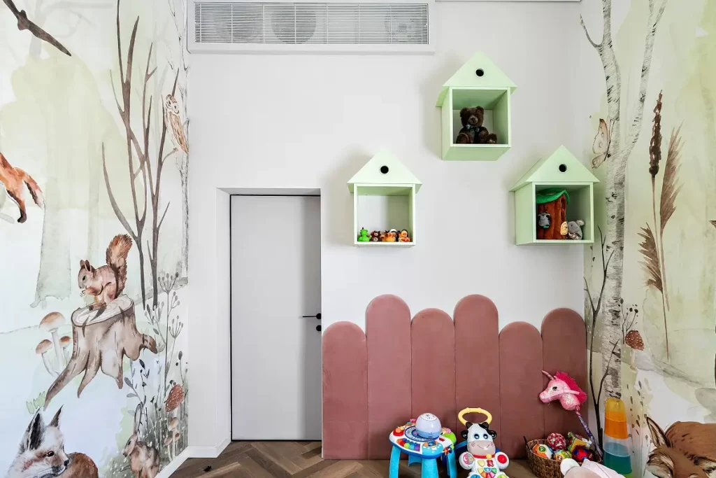 חדר ילדים עם טפט יער, מדפים בצורת בית עם צעצועים, וצעצועים נוספים על הרצפה.
