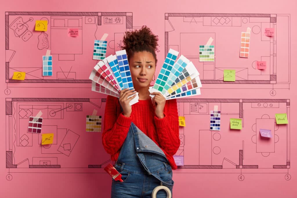 אישה מחזיקה פלטות צבעים ומאחוריה רקע של שרטוט של בית