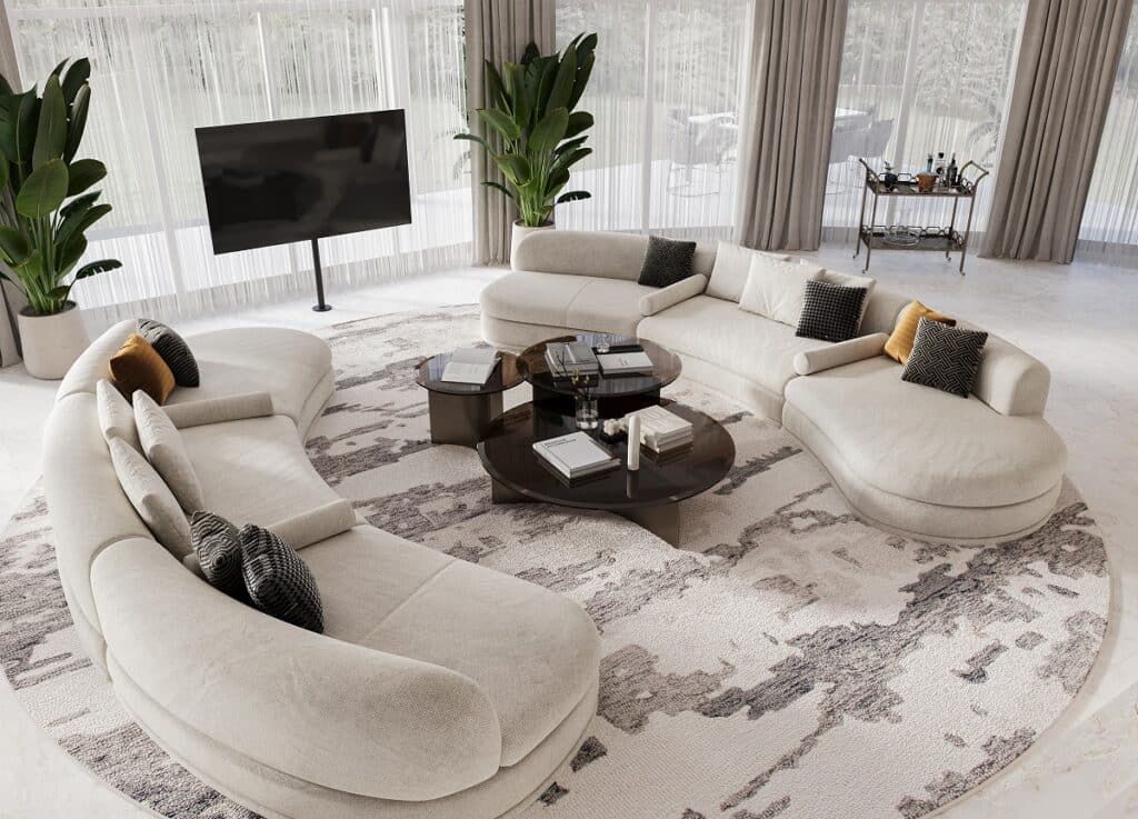 בחדר מרווח עם חלונות גדולים, ספות בהירות מעוגלות מסודרות סביב שולחנות קפה, מול טלוויזיה גדולה וצמחי בית.